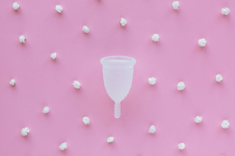 Eco-friendly menstrual cup on a pastel pink background with decorative elements.