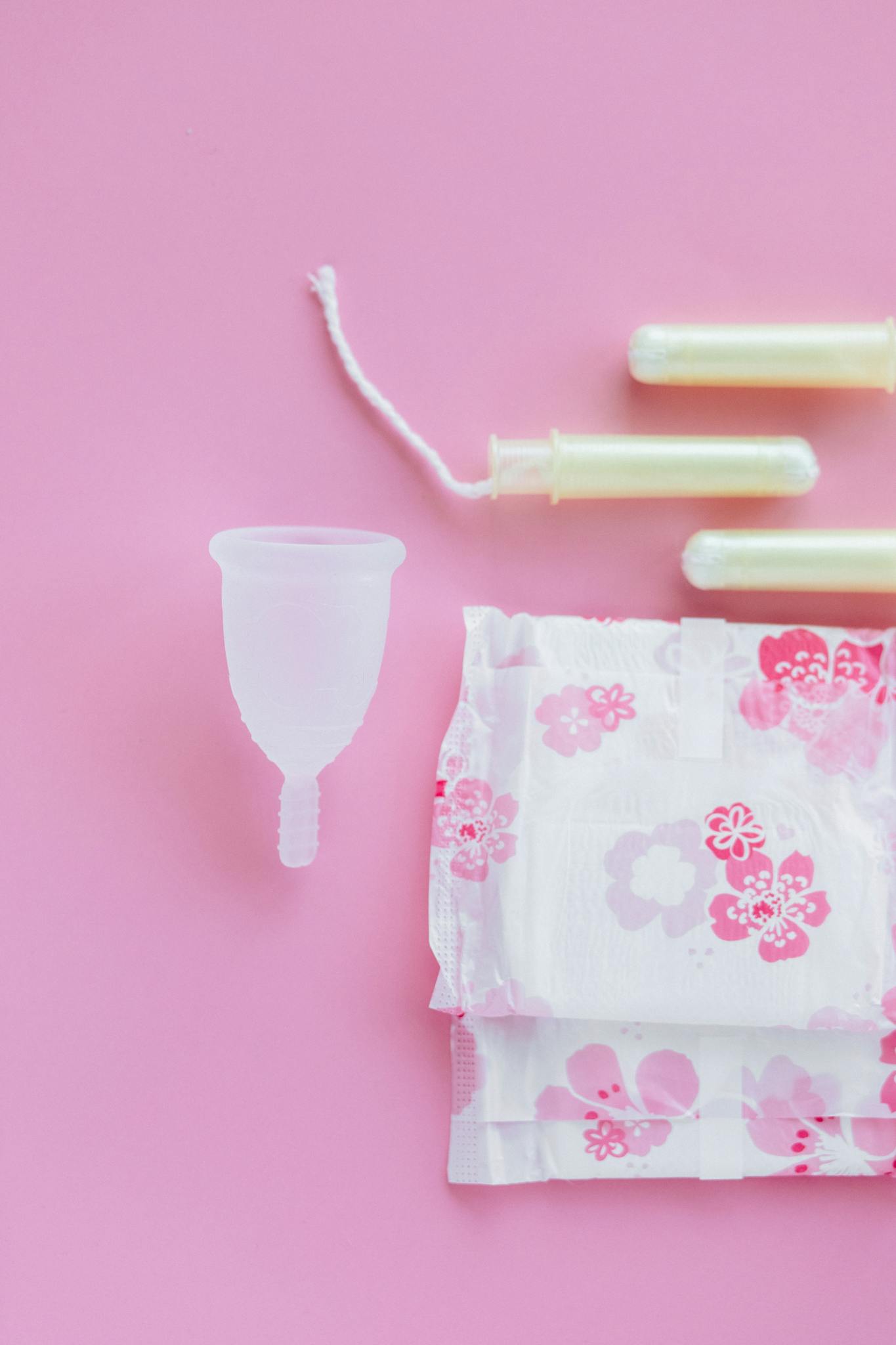 Top view of menstrual cup, pads, and tampons on a pink background.